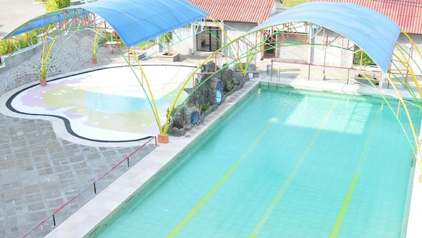 A swimming pool with a tiled deck and a covered area with a roof. - Regina Hotel Pemalang (Pemalang)