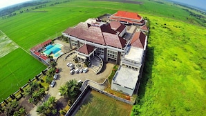 A hotel with a swimming pool, a large parking area, and a view of the surrounding green fields. - Regina Hotel Pemalang (Pemalang)