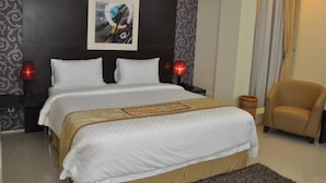A hotel room with a large bed, two bedside lamps, a chair, and a decorative wall piece. - Regina Hotel Pemalang (Pemalang)
