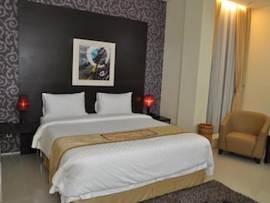 Een hotelkamer met een groot bed, twee bedlampen, een stoel en een decoratief wandobject.