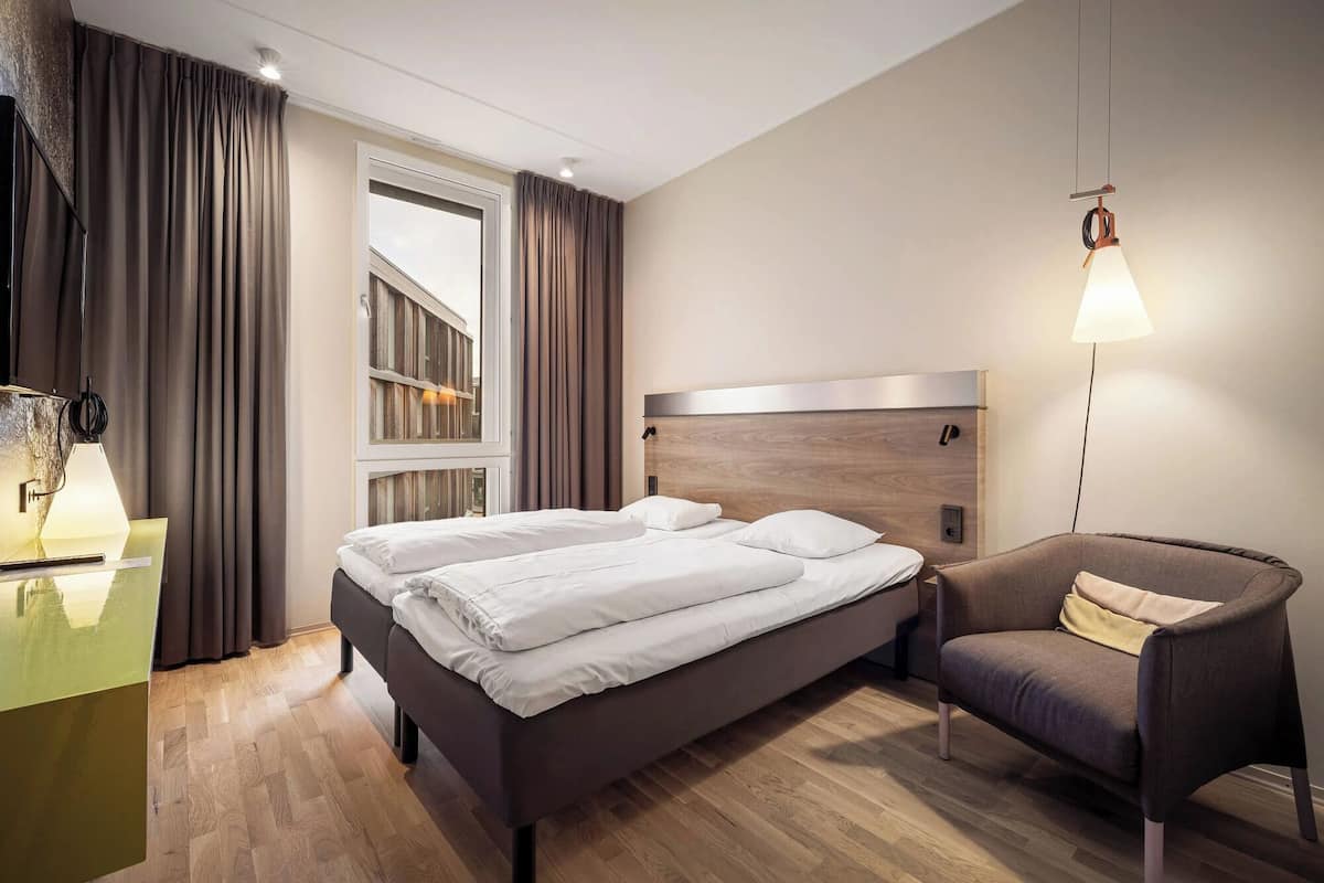 Una habitación de hotel con cama, una silla, un escritorio y una ventana con cortinas.