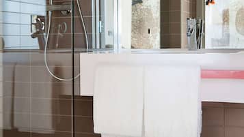 A bathroom with a glass shower enclosure, a white towel hanging on a rack, and a mirror above a sink with a pink soap dish.
