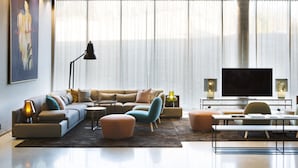 Una sala de estar moderna con un sofá, otomanas, una mesa de centro, un televisor y un cuadro en la pared.