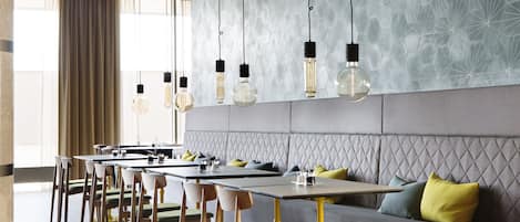 Un comedor moderno con una mesa larga, asientos acolchados, iluminación colgante y un papel tapiz con diseño.
