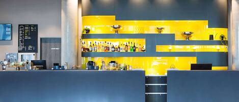 A modern bar area with a yellow and blue color scheme, featuring a counter, shelves with bottles, and a digital display.
