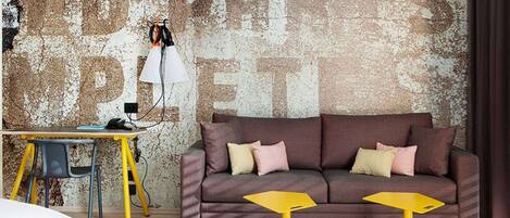 A modern living room with a brown sofa, yellow side tables, and a desk with a lamp.