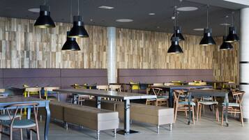 Un comedor moderno con varias mesas y bancos, paneles de madera y luminarias colgantes.