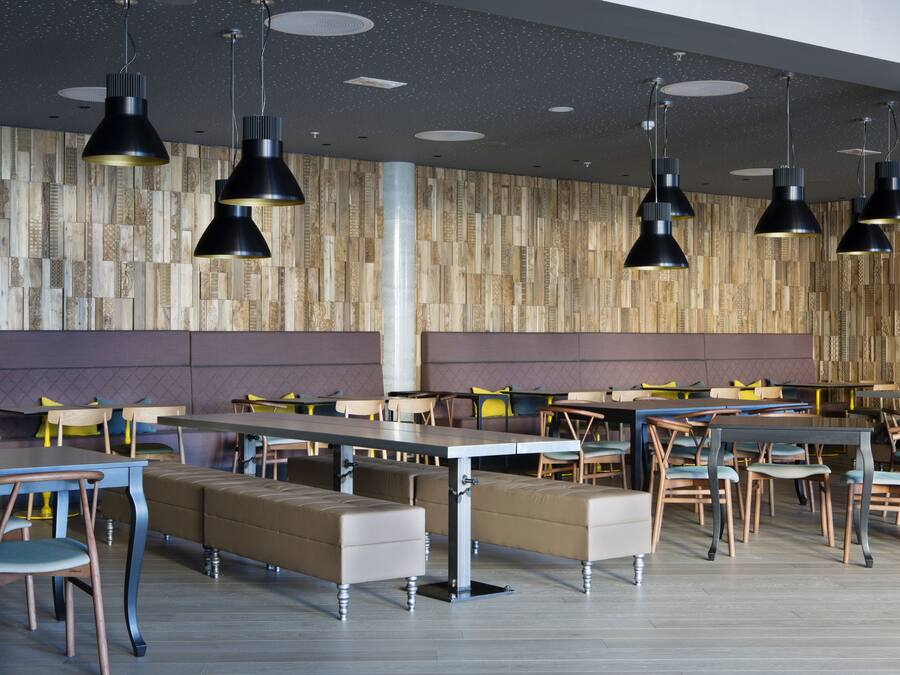 Ein moderner Essbereich mit mehreren Tischen und Bänken, Wandverkleidungen aus Holz und Pendelleuchten.