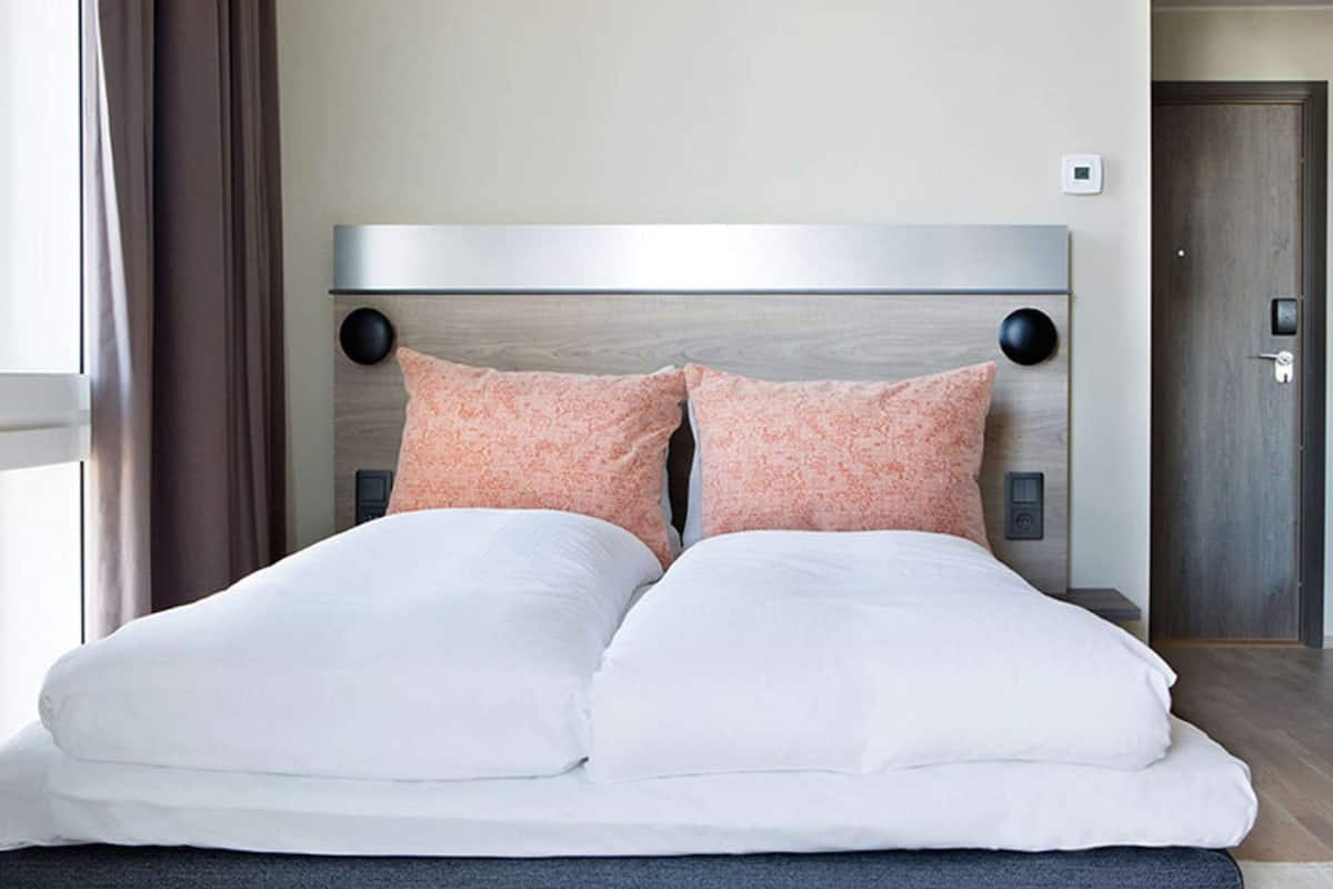Una cama bien hecha con almohadones blancos y melocotón, un cabecero moderno y suelo de madera.