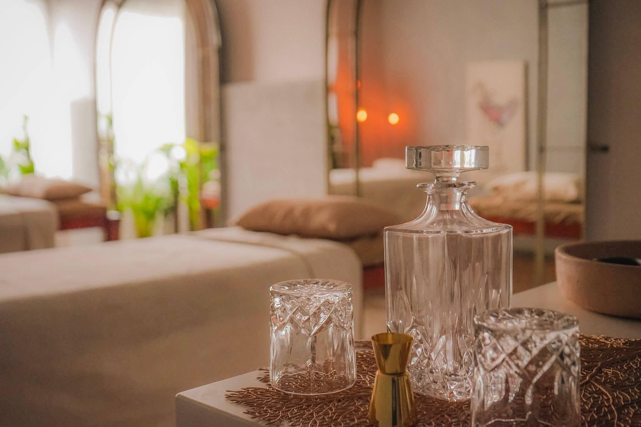 A room with a large bed, a glass bottle, and a small glass on a textured surface.