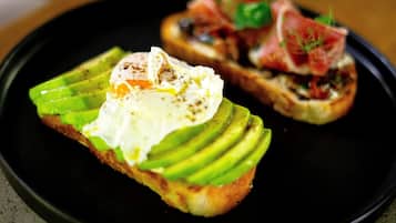 Twee sneetjes geroosterde toast met avocado en gepocheerde eieren op een zwart bord.