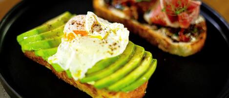 Two pieces of toast with avocado and poached eggs on a black plate.