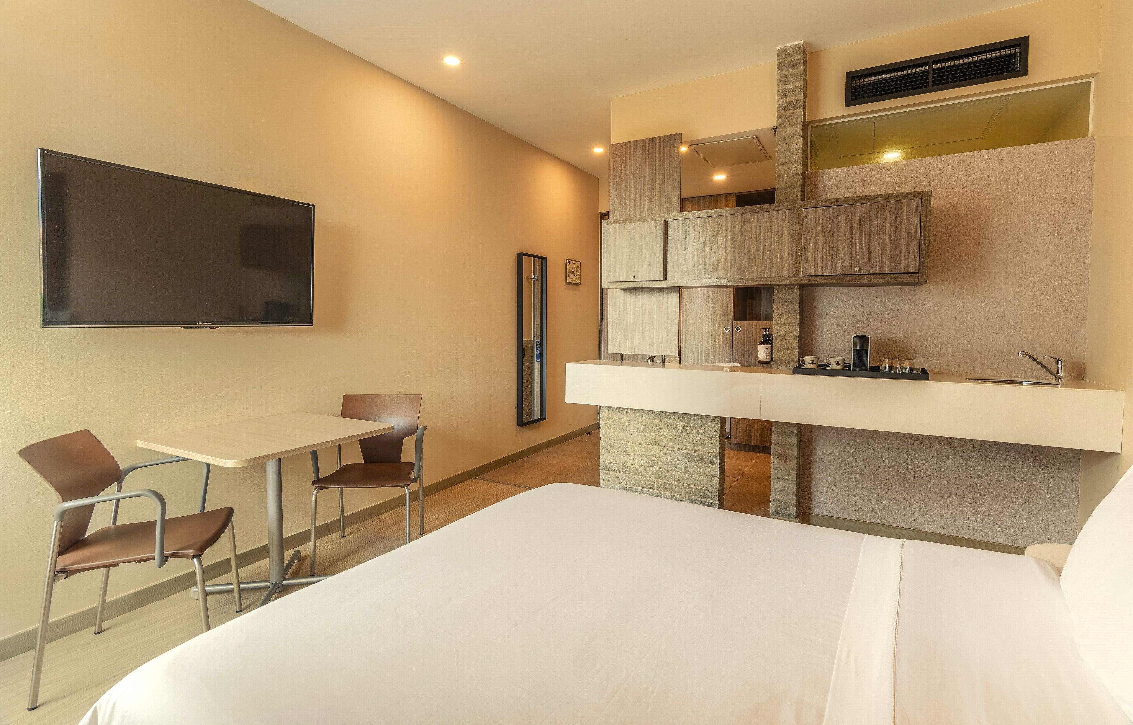 Une chambre d’hôtel équipée d’un lit, d’un bureau, de chaises, d’une télévision, d’une kitchenette et d’un miroir.