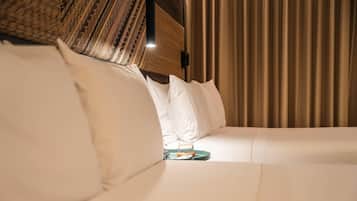 A hotel room with a bed, pillows, a bedside table with a glass, and a curtain.