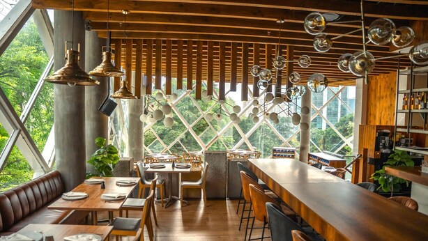 Ein Restaurant mit Holztischen und -bänken, einer Bar und großen Fenstern mit Blick auf Grünflächen.