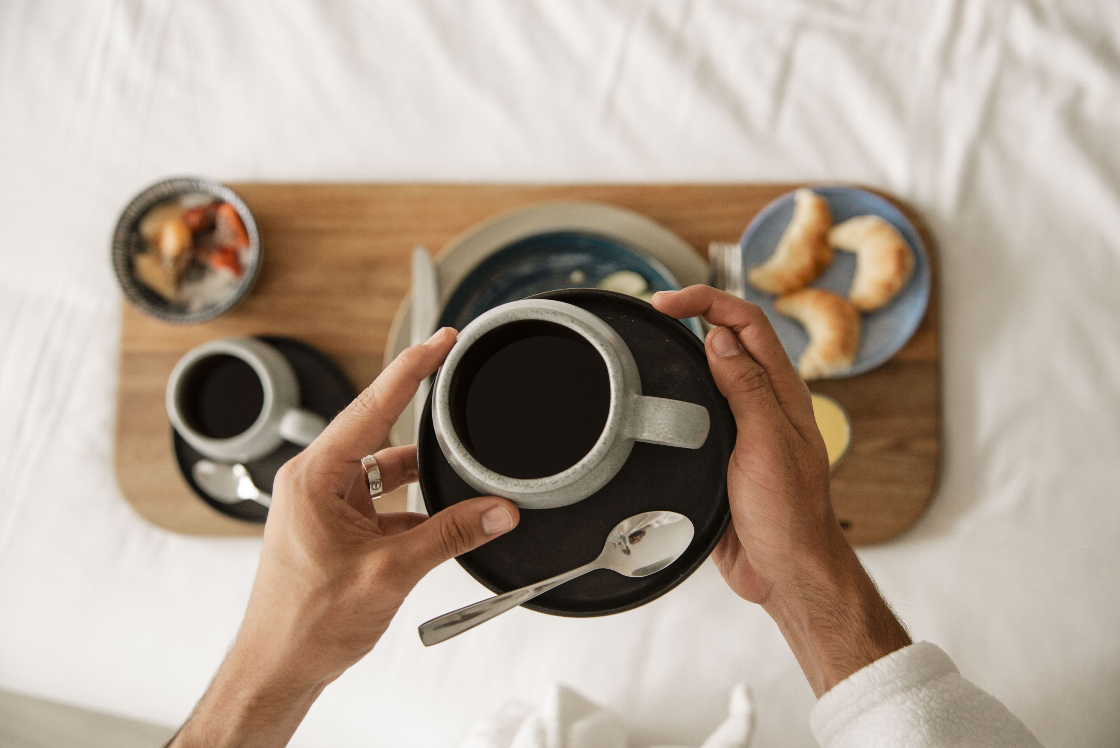 A person holding a cup of coffee with a spoon on a tray.
