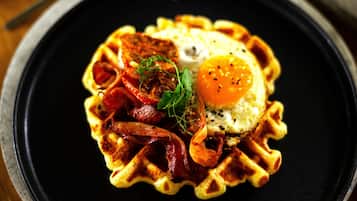 A waffle with a fried egg and bacon on a black plate.
