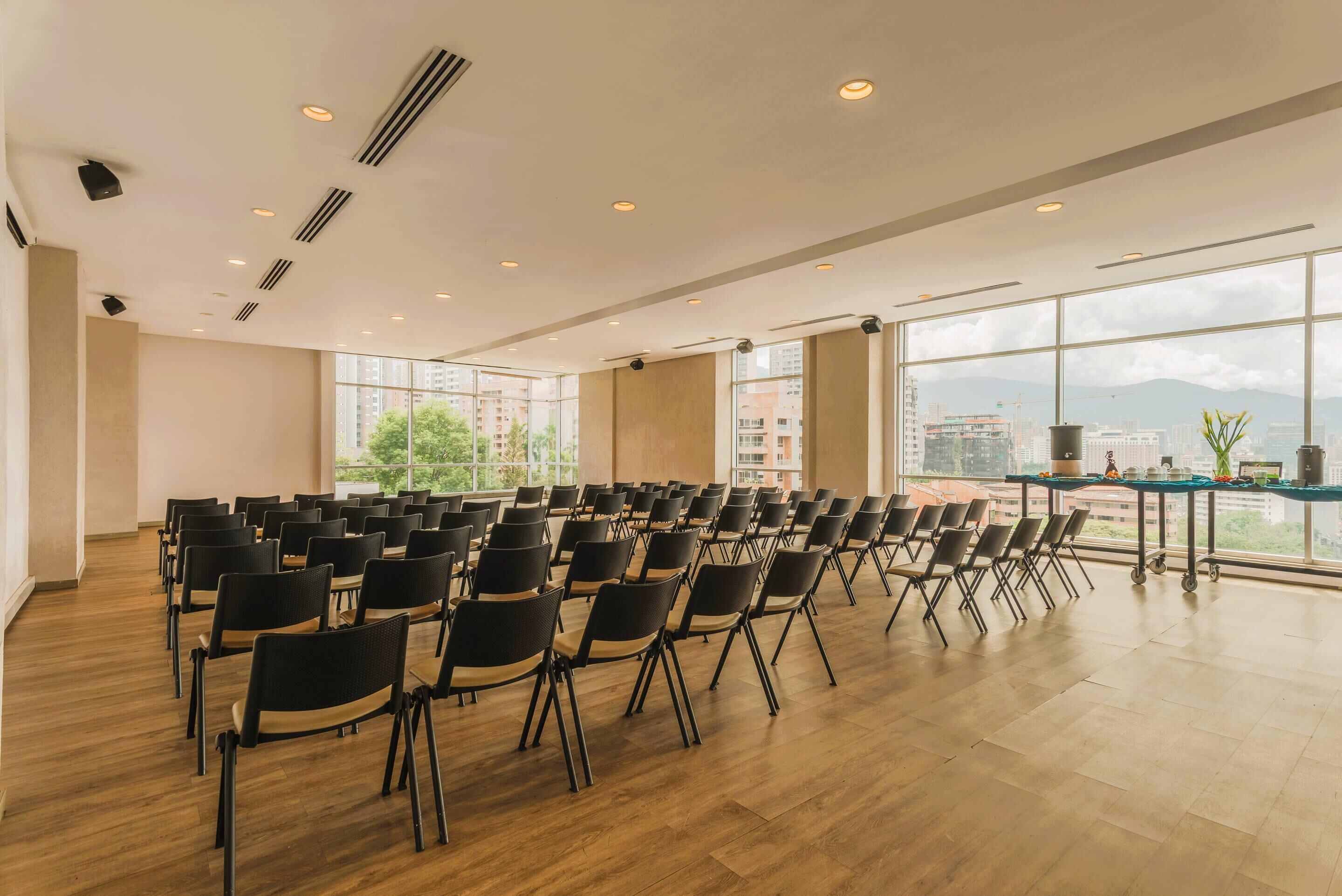 A conference room with rows of chairs, large windows, and a city view.