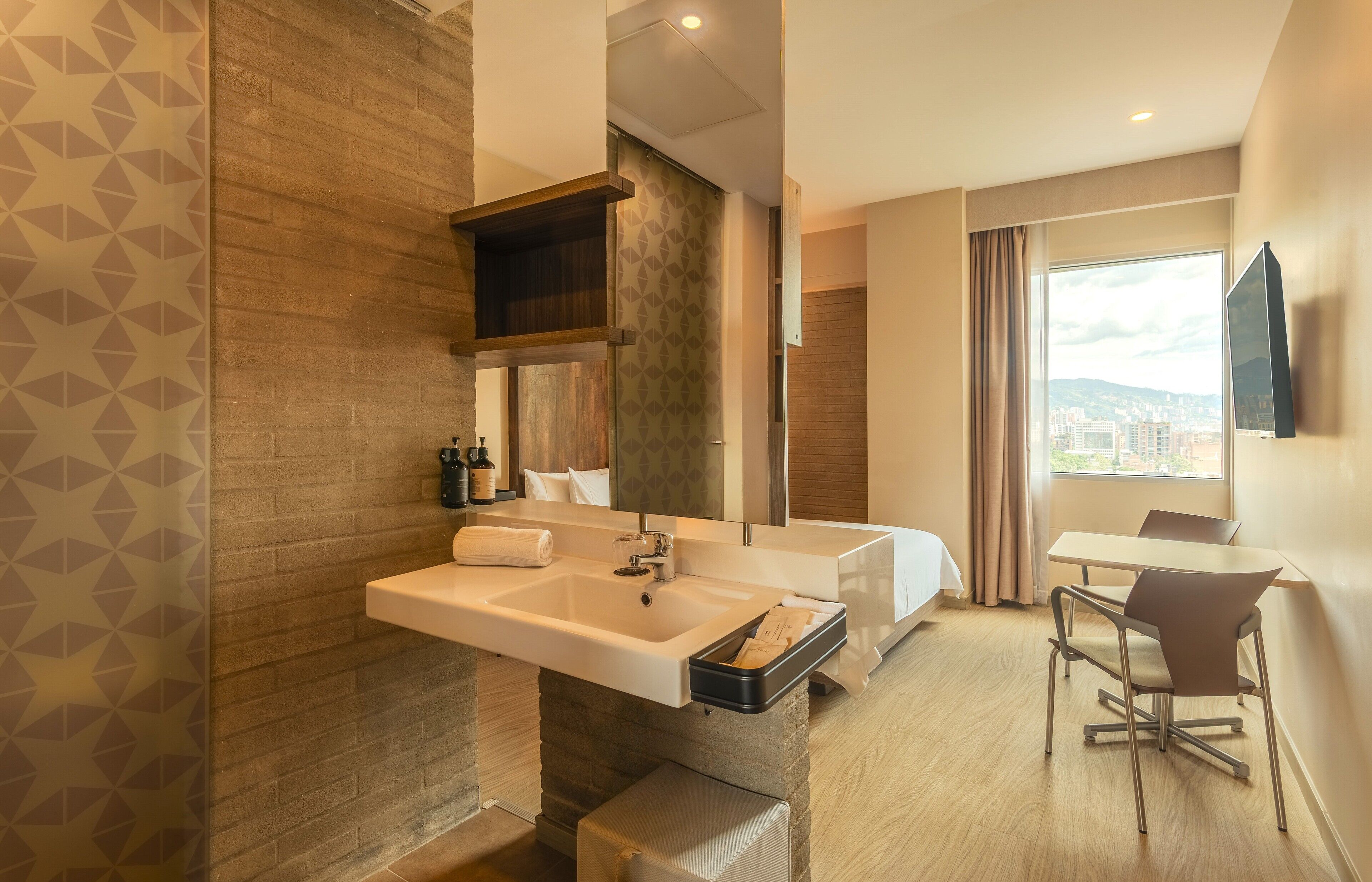 Ein modernes Badezimmer mit einem großen Waschbecken, einem Spiegel, einer Duschkabine und einem Fenster mit Blick auf die Stadt.