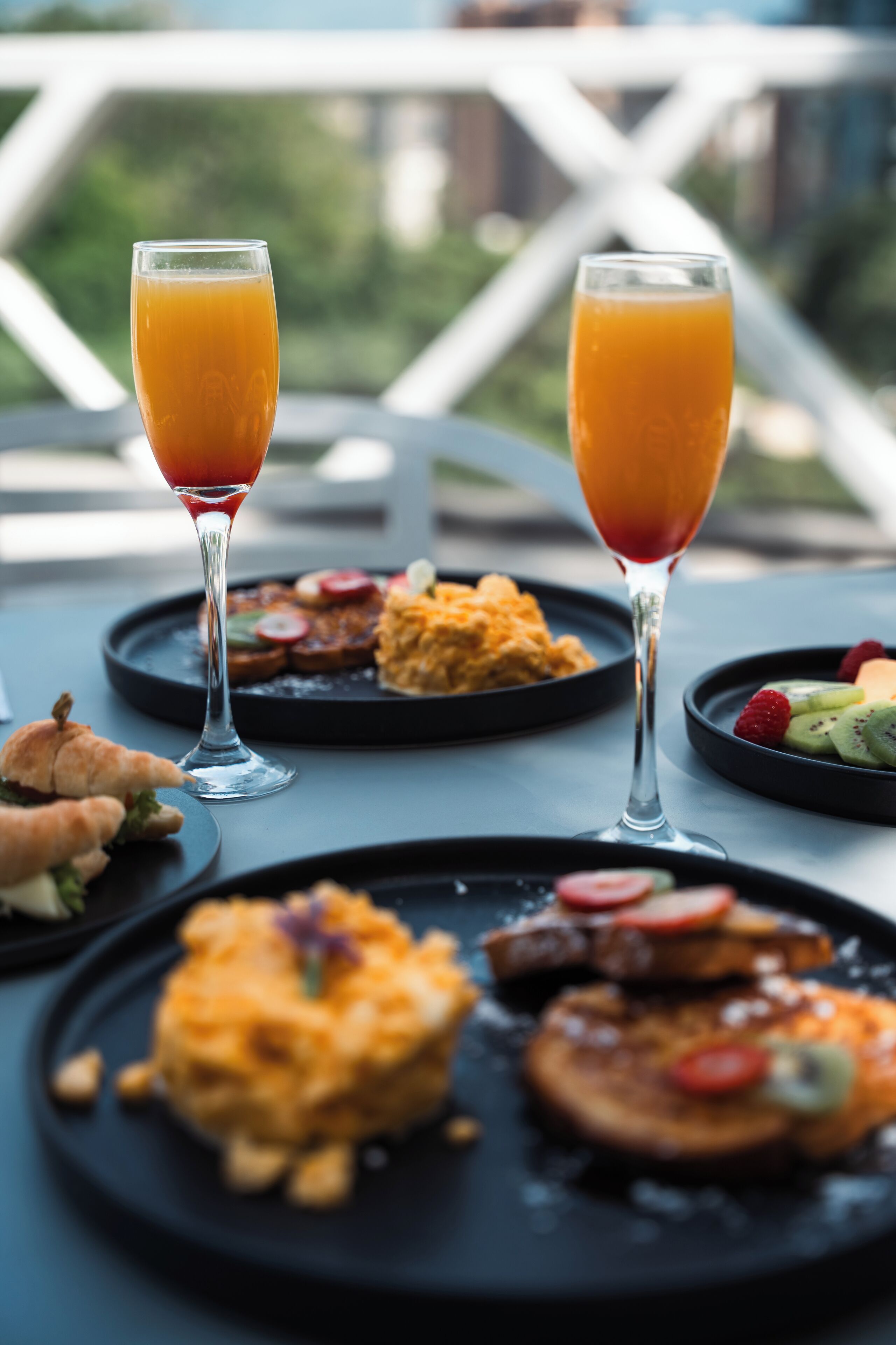 Une table de petit-déjeuner avec deux verres de jus d’orange, une assiette d’œufs brouillés et une autre avec des fruits et des noix.