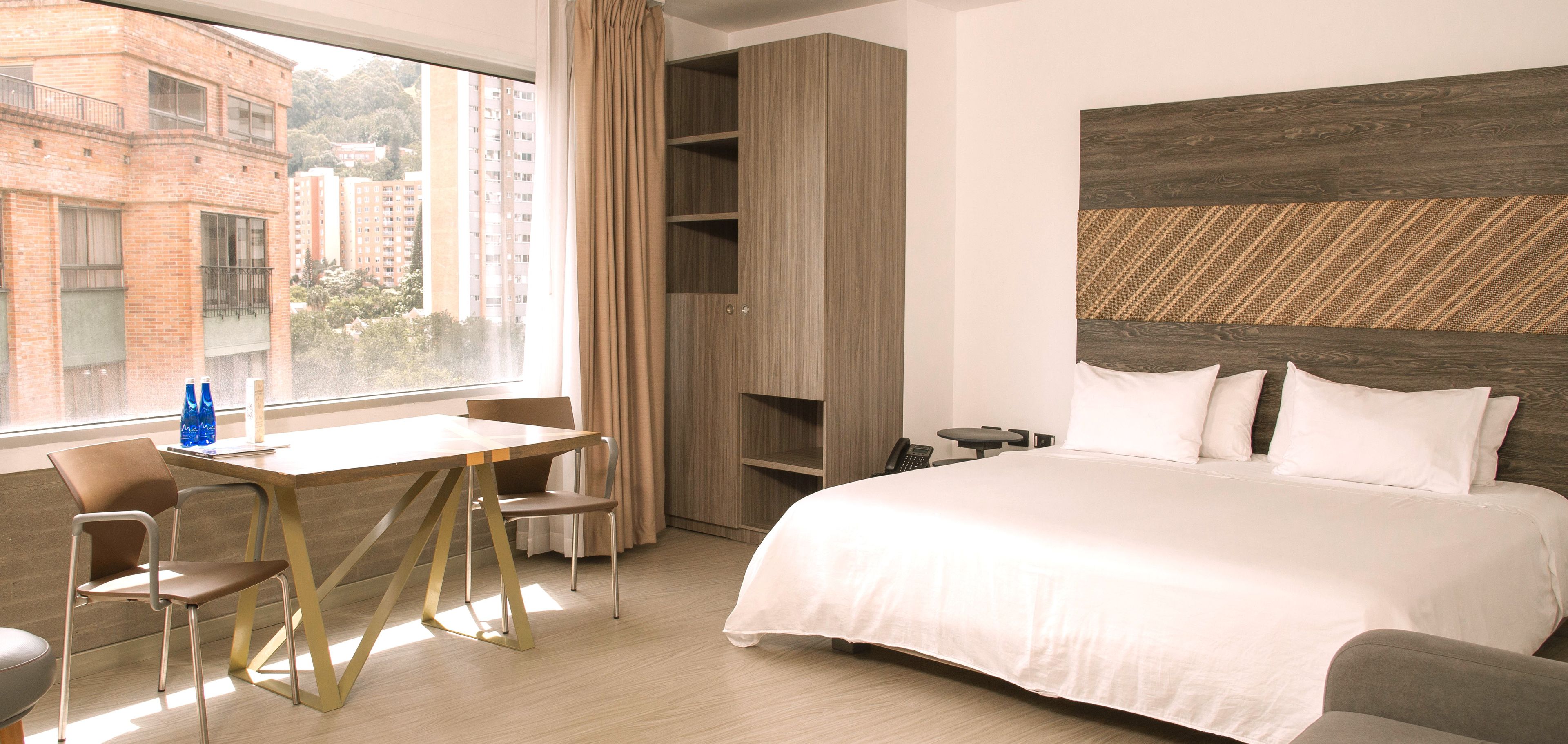 Habitación de hotel con cama, escritorio con sillas, teléfono y vistas a edificios.