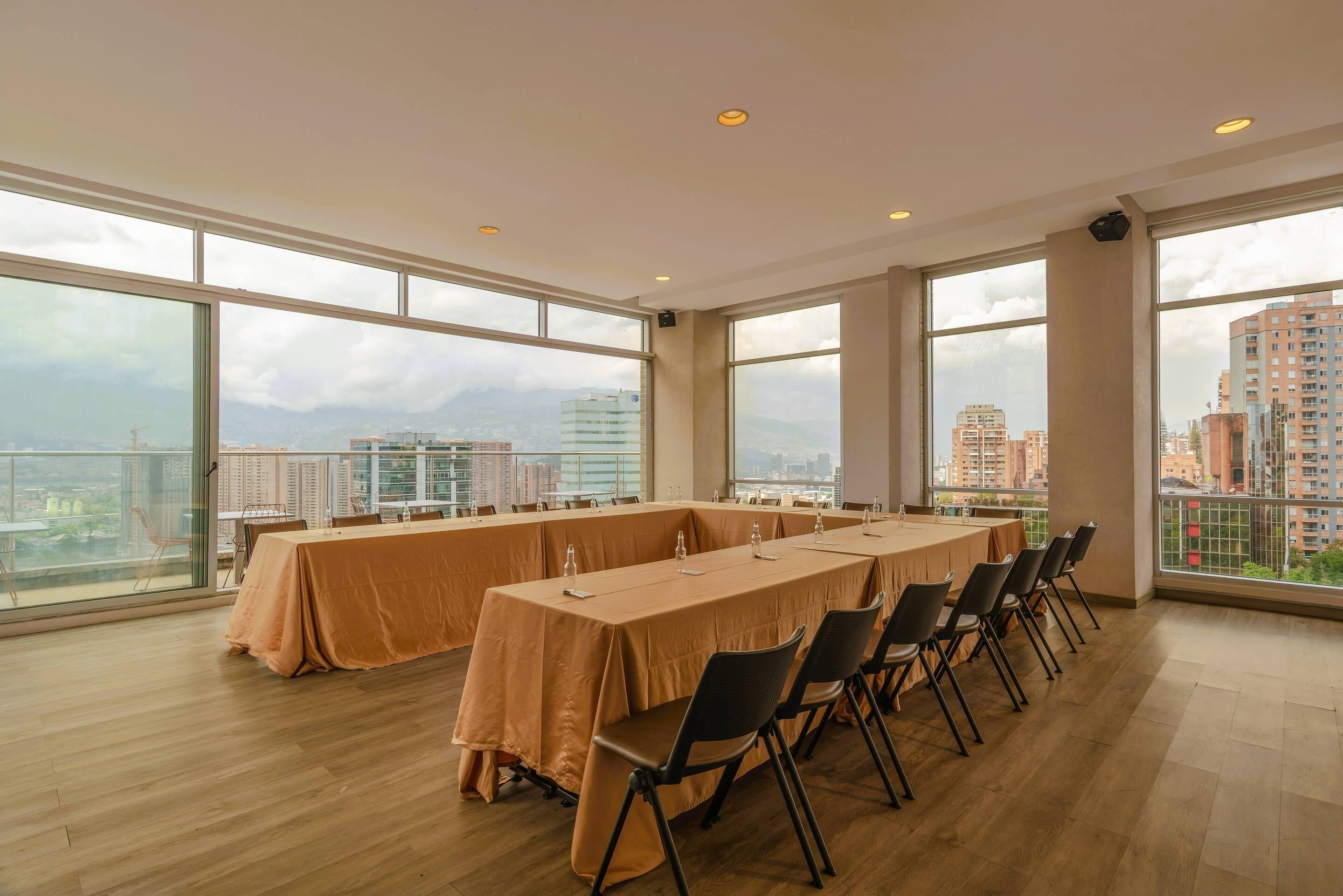 A conference room with a long table, chairs, and large windows offering a city view.