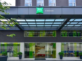 Una entrada de hotel moderna con un letrero verde, amplias ventanas y un área de acceso cubierta.