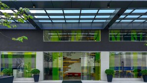 Een moderne hotelentree met een groen bord, grote ramen en een overdekt gebied.
