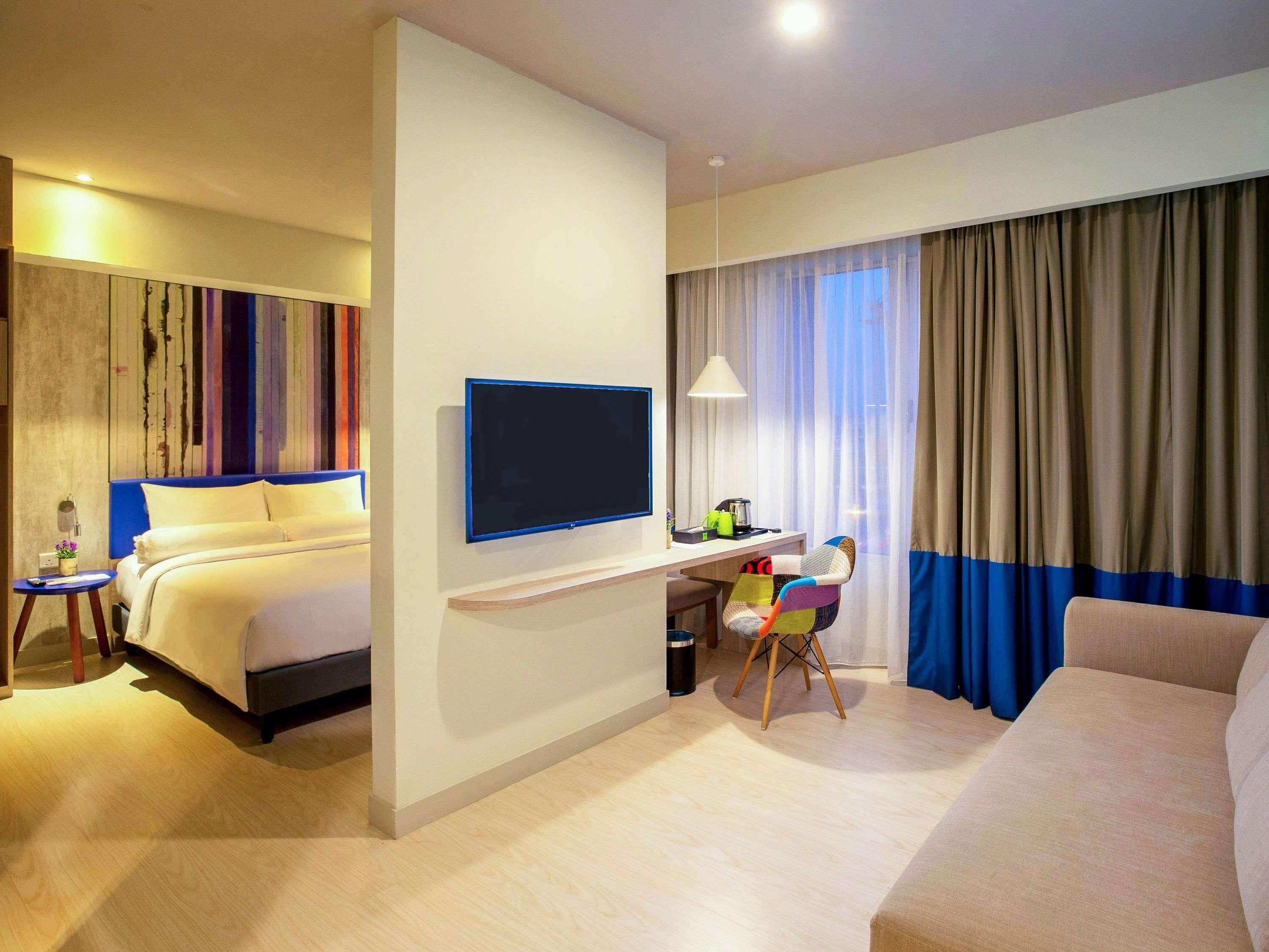 Una habitación de hotel con cama, escritorio con silla, televisor y sofá.