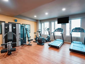 Une salle de sport équipée de machines de cardio, d’appareils de musculation et d’un écran de télévision.
