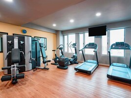 A gym with cardio machines, weight training equipment, and a television screen.
