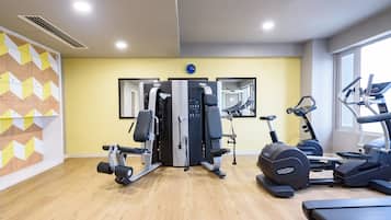 Un gimnasio con máquinas de cardio, una banca de pesas y un espejo grande.