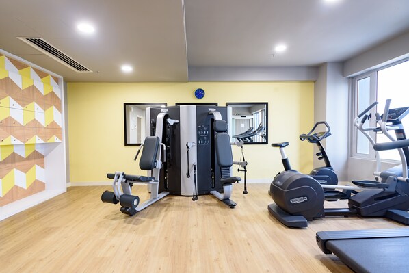 Ein Fitnessraum mit Laufbändern, einer Gewichtbank und einer Spiegelwand.