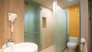 Un baño con cabina de ducha de vidrio, inodoro con pared de azulejos amarillos y lavamanos con secador de pelo montado en la pared.