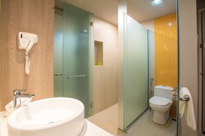 Un baño con cabina de ducha de vidrio, inodoro con pared de azulejos amarillos y lavamanos con secador de pelo montado en la pared.