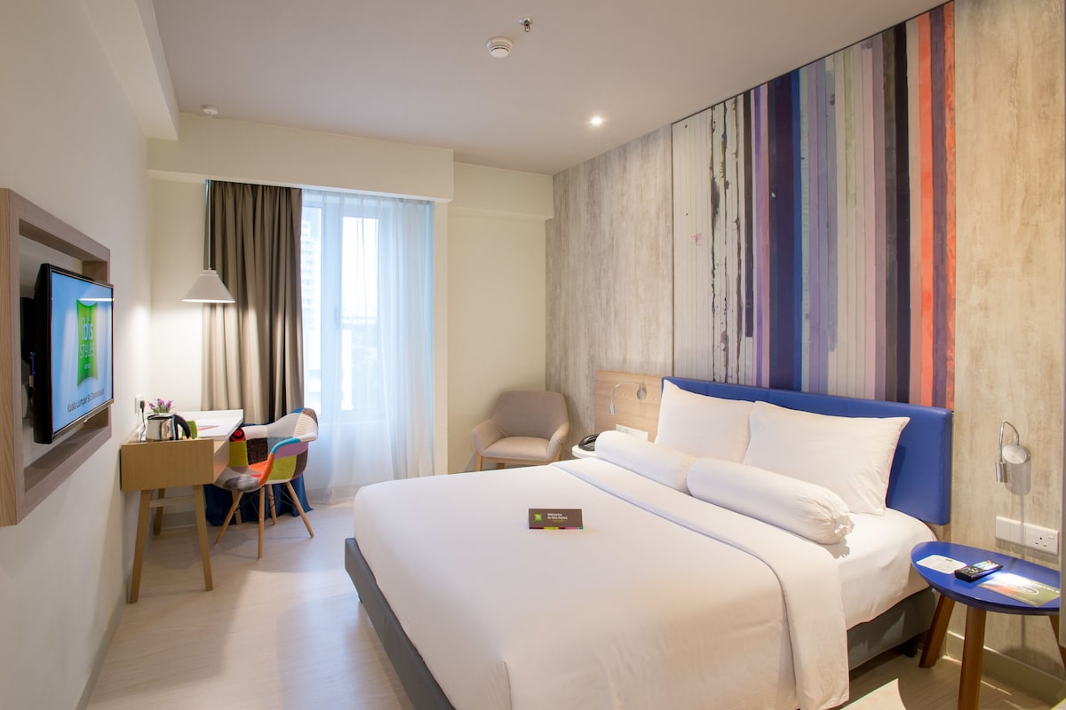 Habitación de hotel con una cama grande, un escritorio con silla, un televisor y una pared de colores.