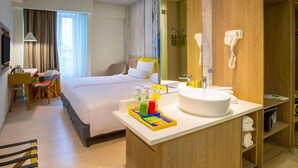 Een hotelkamer met een bed, een bureau, een stoel, een badkamer met een wastafel en een spiegel.