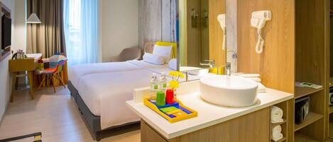 Habitación de hotel con cama, escritorio, silla y baño con lavabo y espejo.