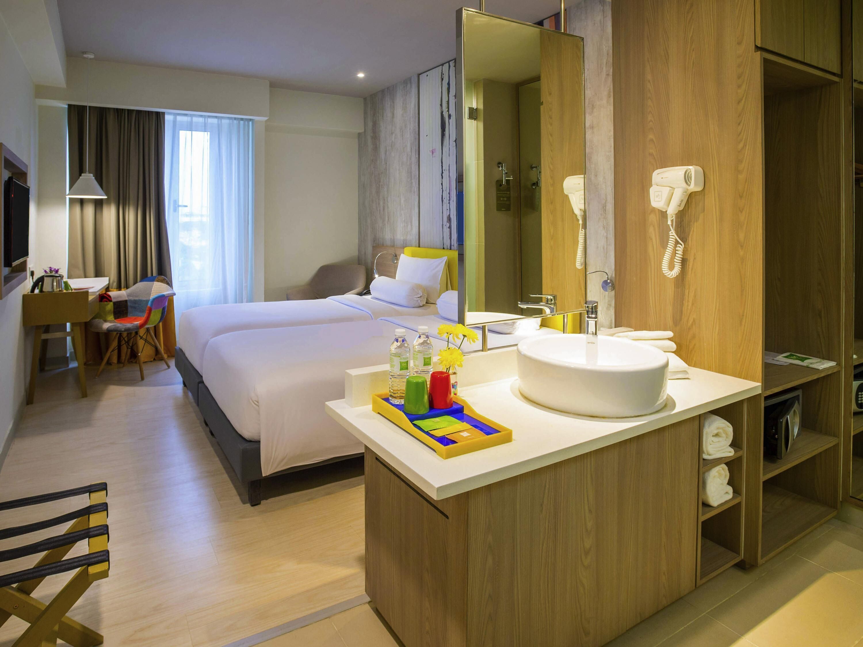 A hotel room with a bed, a desk, a chair, a bathroom with a sink and mirror, and a wardrobe.