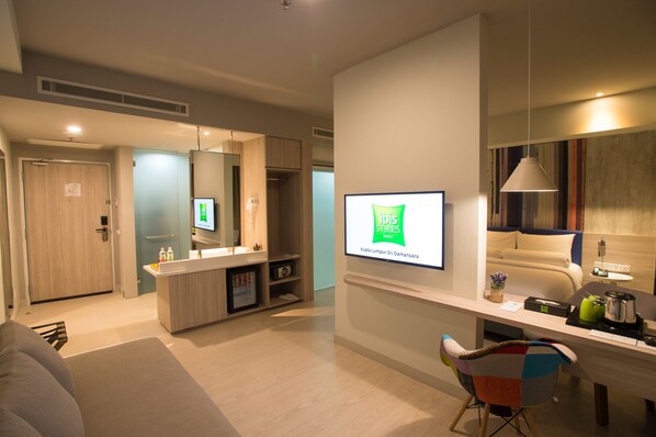 A modern hotel room with a large mirror, a flat-screen TV, a desk with a chair, and a sofa. - ibis Styles Kuala Lumpur Sri Damansara (Batu Caves)