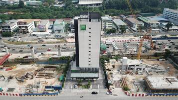 A multi-story hotel with a prominent green logo, surrounded by construction sites and busy roads.