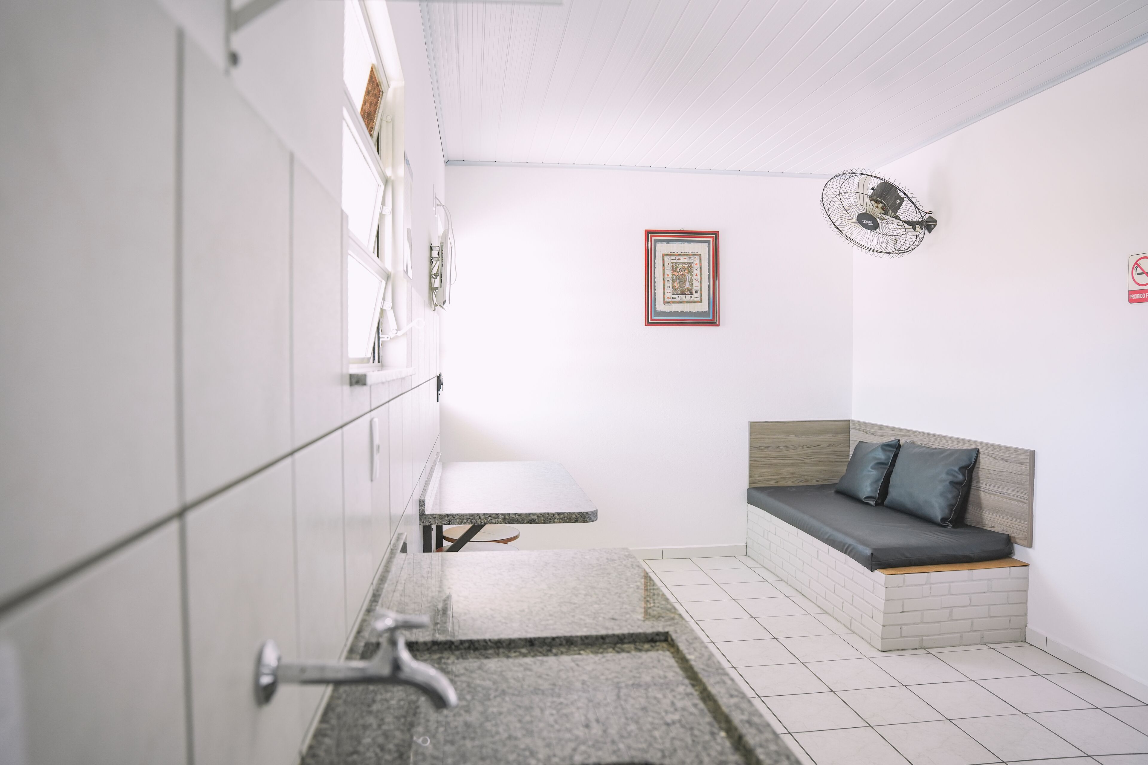 Une petite pièce comprenant un lit, une petite table et un ventilateur fixé au mur.