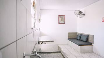 Une petite pièce comprenant un lit, une petite table et un ventilateur fixé au mur.