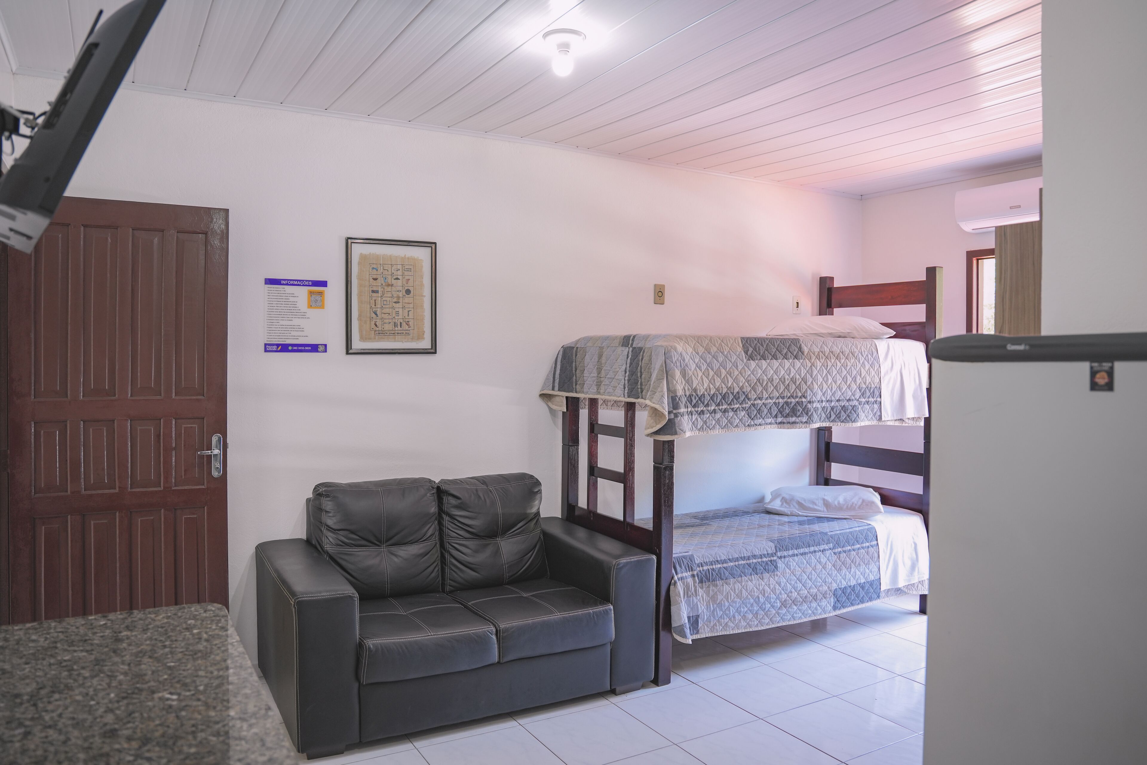 Una habitación con una cama litera, un sofá, una puerta y una lámpara fijada a la pared.