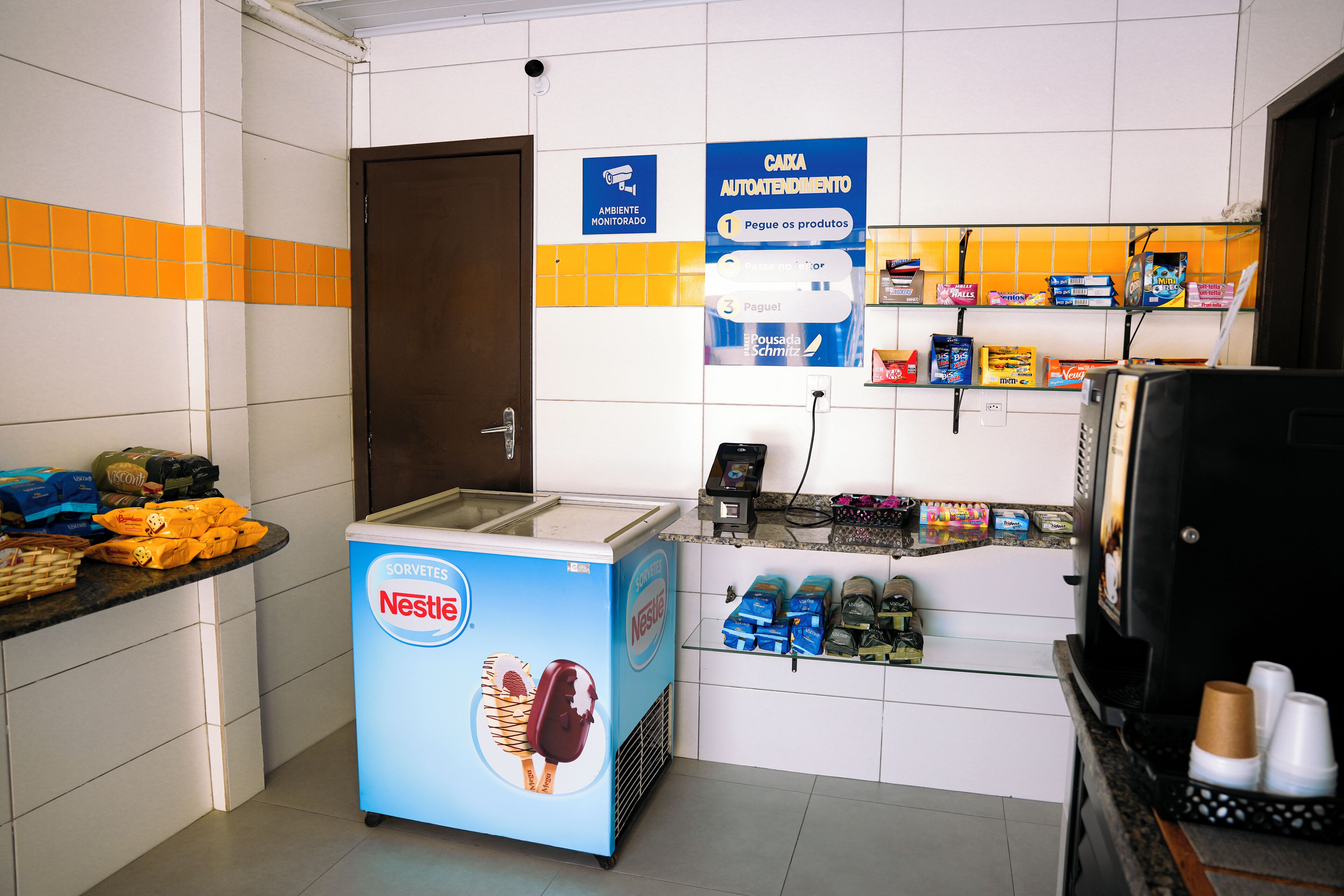 A small ice cream freezer with a Nestle advertisement, a counter with various snacks, and a sign for a monitored cash box.