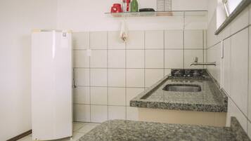 A small kitchen with white tiles, a granite countertop, a stainless steel sink, and a white refrigerator.