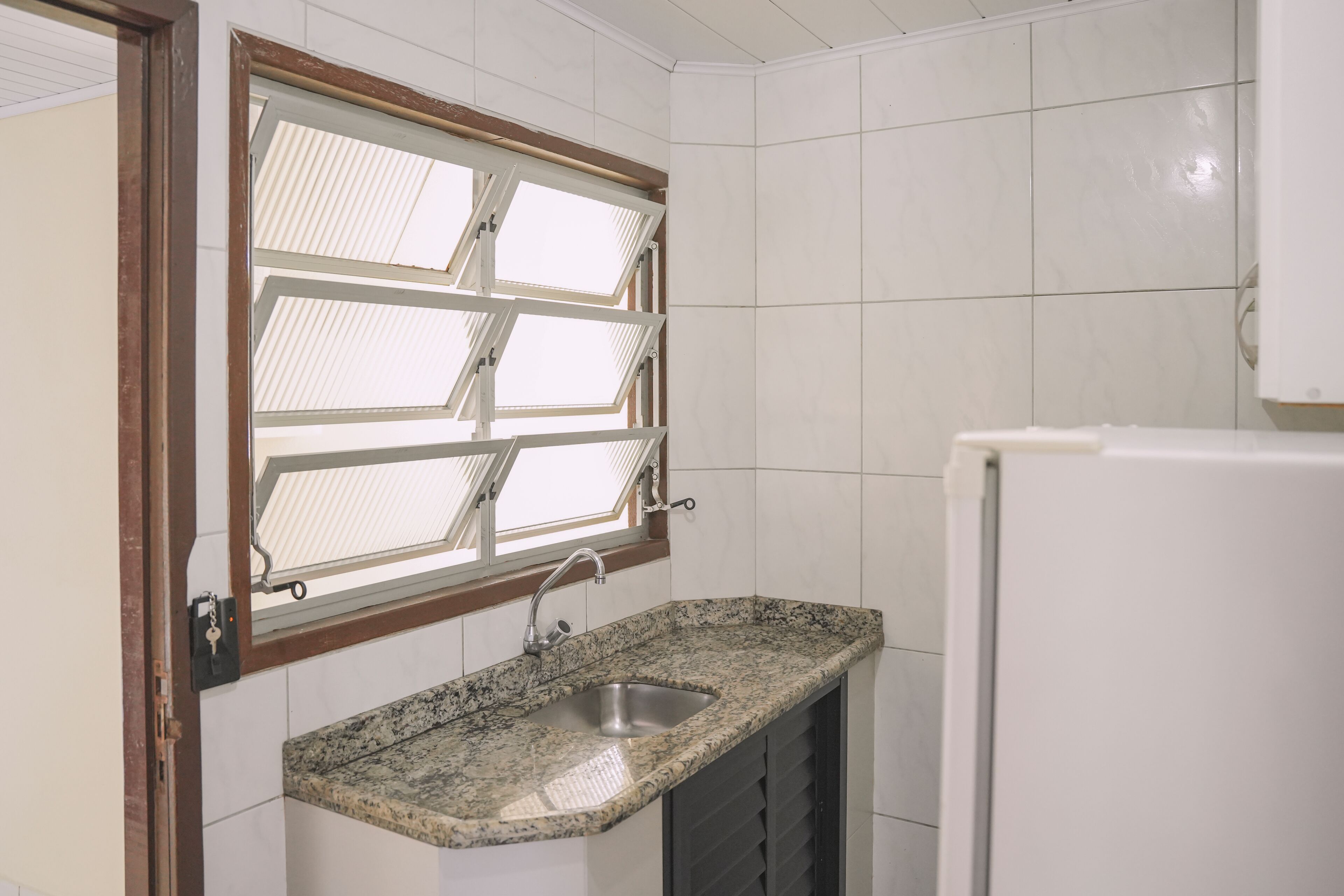 A small kitchen with a granite countertop, a stainless steel sink, and a window with blinds.