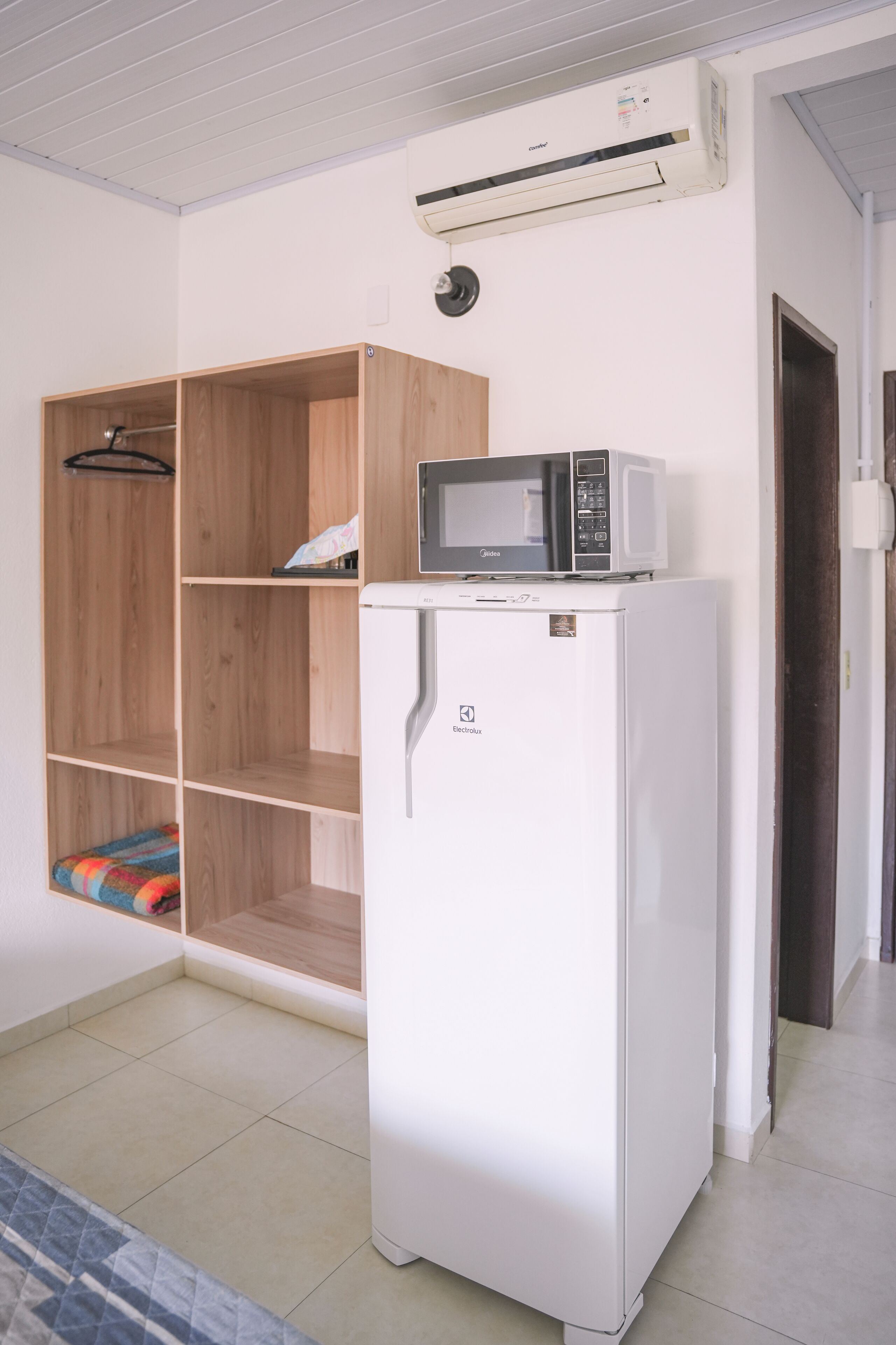 Une pièce de taille modeste, avec un réfrigérateur blanc, un four à micro-ondes posé sur le dessus, une armoire en bois et un sol carrelé.