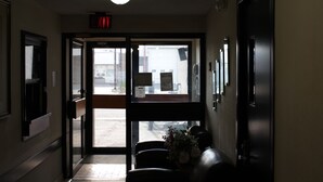 A hotel lobby with a reception desk, a glass door leading outside, and an exit sign above the door. - Morinville Plaza & Suites (Morinville)