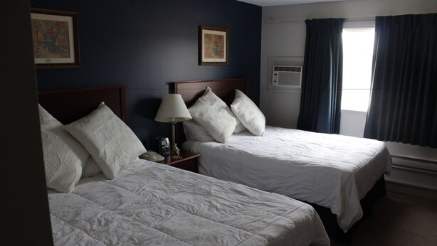 A hotel room with two beds, a nightstand with a lamp, and artwork on the walls. - Morinville Plaza & Suites (Morinville)